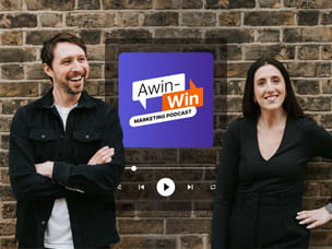 Two Awin employees standing in front of a  brick wall featuring Awin's podcast advertisement.
