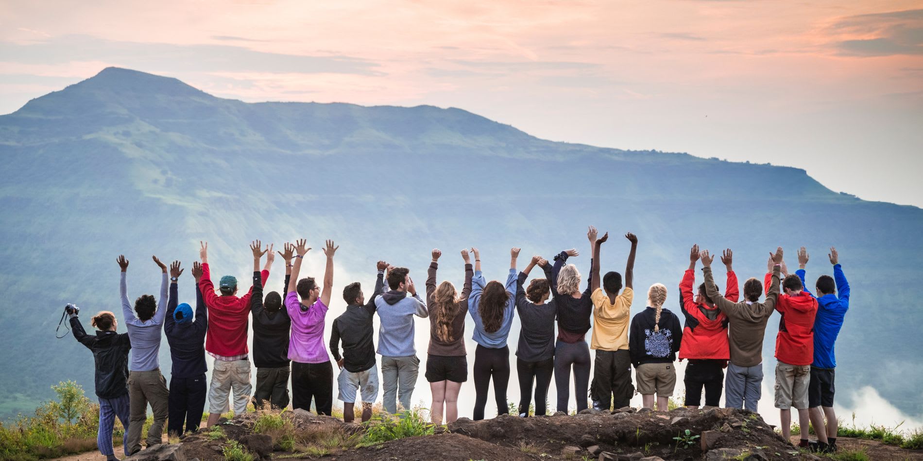UWC students of many nationalities with hands up in the air and backs to the camera facing a mountain