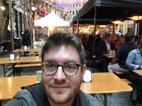 a selfie of Marty seated in a cluster of empty tables, next to a cluster of crowded ones