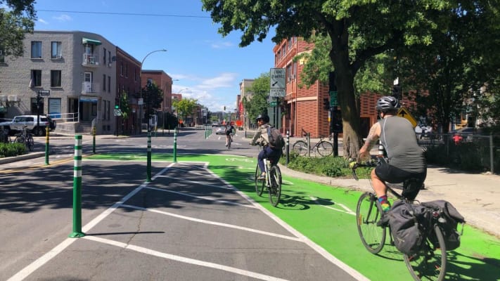 Two cyclists riding on the Bellechasse EBN, on a section painted green to delimit a protection zone at the intersection.